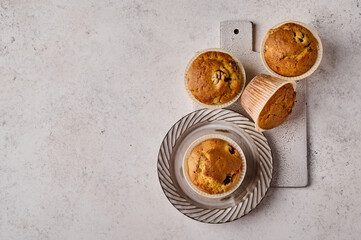 Top view cupcakes in baking paper forms on plate and scratched ceramic cutting board on gray background, copy space