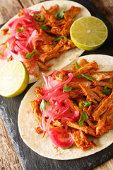 Cochinita pibil also puerco pibil or cochinita con achiote is a traditional Mexican slow-roasted pork dish from the Yucatan closeup in the slate board on the table. Vertical
