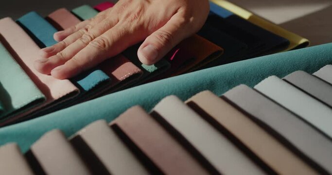 The tailor runs his hand over samples of multi-colored fabric. Selection of materials for fashion clothes