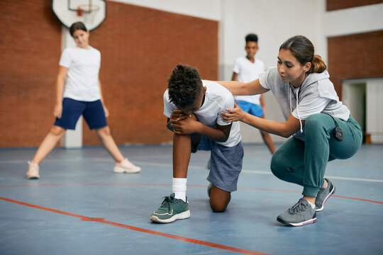 Sports Teacher Helps Black Elementary Student Who Has Injured His Leg During PE Class At School Gym.