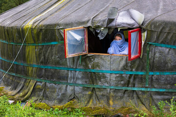 Young blue-eyed girl with headscarf leaning out of the window of a Mongolian tent.
