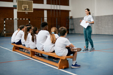 Happy physical education teacher talks to her students during class at elementary school gym.