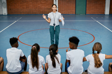 Young sports teacher communicates with group of school kids during physical education class.