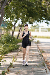 A healthy happy Asian woman runner in black sport outfits jogging in the natural city park under evening sunset