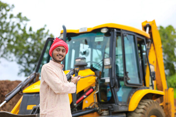 Indian farmer standing with his new earth mover machinery.