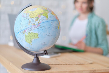 blurred globe in the foreground. in the background a woman works at a laptop, illustration of an international company or online profession. freelancer works remotely