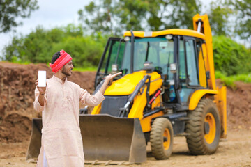 Indian farmer showing smartphone with his new earth mover machine equipment