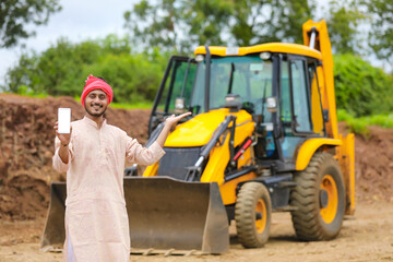 Indian farmer showing smartphone with his new earth mover machine equipment