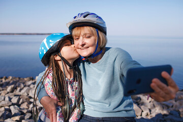 Happy senior woman taking selfie together with grandchild after riding on roller skates, hugs and support, family activity, spring or fall outdoors, healthy lifestyle