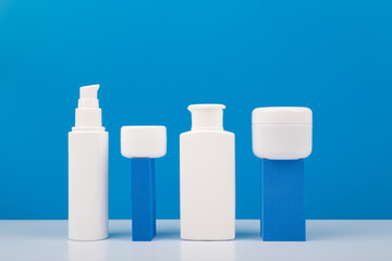 Set of white unbranded cosmetic bottles for daily skincare on geometric props for product presentation against bright blue background. Concept of hygiene, man's skin care or anti acne treatment