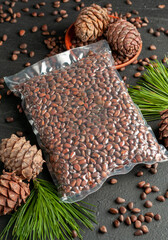 Vacuum packed pine nuts in shell. Nearby are pine cones, nuts and needles. Dark background. View from above.