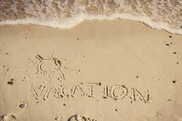 Inscription vacation with shape of sun and incoming sea wave on sand at beach. Summer time
