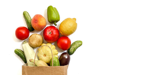 A paper shopping bag with vegetables and fruits, tomato, cucumber, squash, pepper, lemon, eggplant, zucchini, banana, apple, peach on white background
