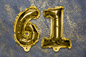 The number of the balloon made of golden foil, the number sixty-one on a gray background with...