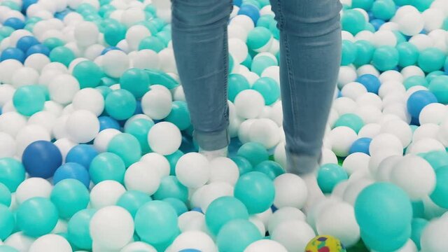 A girl in jeans and white socks throws plastic balls in different directions. Close up video