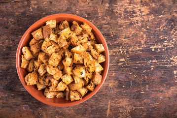 Fried ciabatta croutons in a clay plate on an outdoor wooden table, top view, copy space