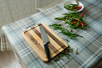 Cutting hot red and green chili peppers with a knife on a cutting board in a home kitchen in natural daylight
