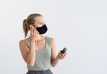 Young woman in a protective mask holding wireless earbuds