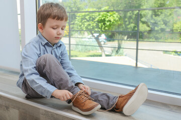Cute little boy tying shoe laces at home, space for text