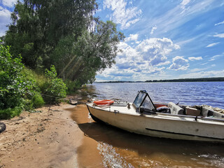 Fototapeta na wymiar old motor boat on sandy shore with beautiful green summer landscape