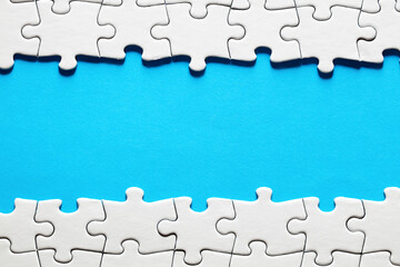 Blue background surrounded by white jigsaw puzzle pieces with copy space.
