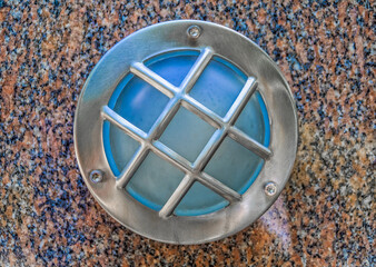 Circle outdoor wall lamp with aluminium guard. It is mounted on granite wall.