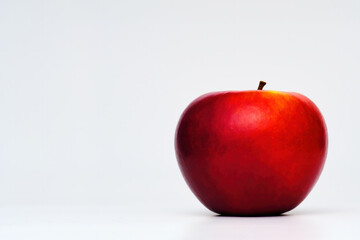 a fresh red apple isolated in graduated white background with back lighting and some dark shade of shadow
