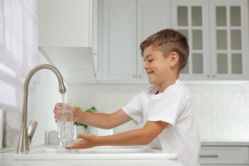 Boy filling glass with water from tap in kitchen