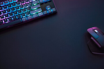 Top down view of dark grey desk with colorful illuminated gaming accessories.