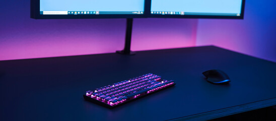 Gaming place. Large dark desk with wireless illuminated keyboard and mouse. Dual monitor on stand.