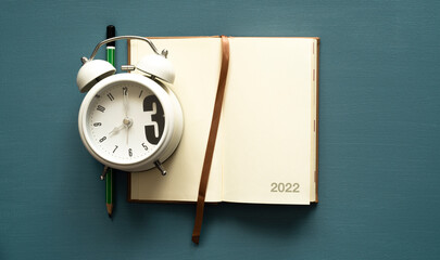 calendar 2022 with space for text, notebook, brown tab, green pencil, white clock, on a painted background, photo from above
