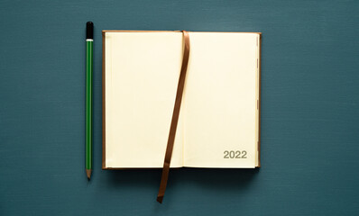 2022 calendar with space for text, notebook, brown tab, green pencil, on a painted background, photo from above