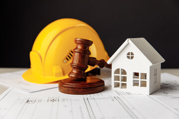 Wooden gavel, house and yellow helmet on construction plan