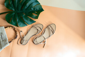 Top view of monstera palm leaf, luxury sandals and raffia bag on two beige tone  background. Concept for summer times and vacation.