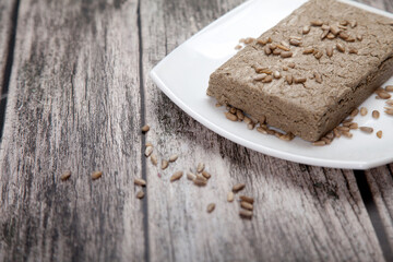 Sunflower seed halva lies on a white porcelain plate on a wooden background.