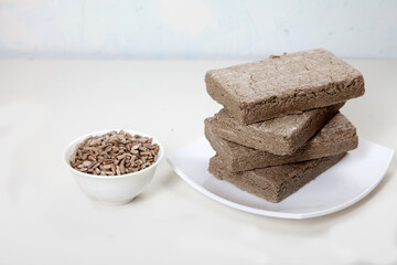 Briquettes of halva from sunflower seeds are on a white plate. Sunflower seeds in a porcelain cup are next to each other.