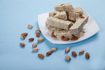 Halva made from sunflower seeds, almonds and pistachios lies on a plate against a blue background. Pistachios and almonds are scattered side by side.