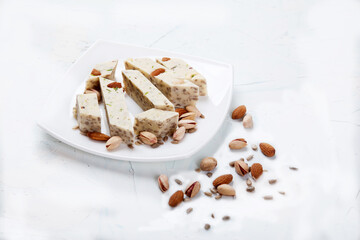 Halva made from sunflower seeds, almonds and pistachios lies on a plate on a white background. Copy spaes.