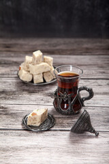 Turkish glass of tea and sunflower halva with almonds and pistachios stands on a wooden background.