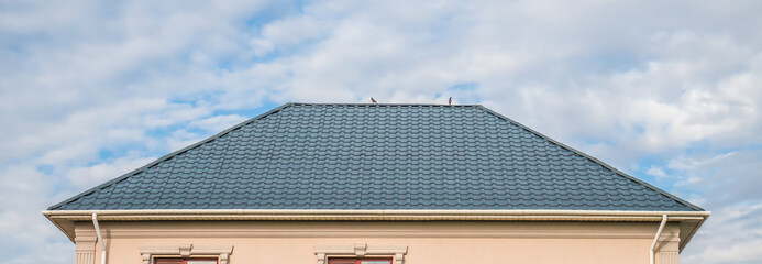 The roof is made of metal. Metal roofing sheets. Modern types of roofing materials. House roof, metal tiles against the blue sky. - obrazy, fototapety, plakaty