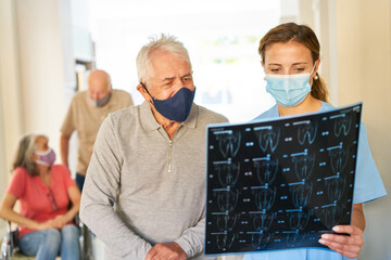 Senior Patient und Ärztin mit Mundschutz betrachten ein MRT
