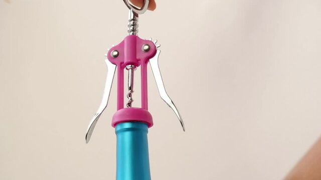 A woman's hand with an opener opens a wooden cork from a bottle of wine (alcoholic drink) on a beige background. Close-up