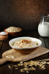 Oatmeal porridge with almonds next to ear of oats lying on the cutting board. Healthy eating. Vegan and vegetarian food. Vertical orientation, copy space.