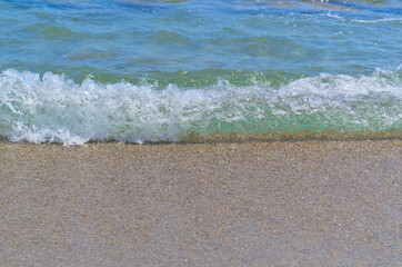 Summer background. Blue sea wave with foam on the sandy shore.