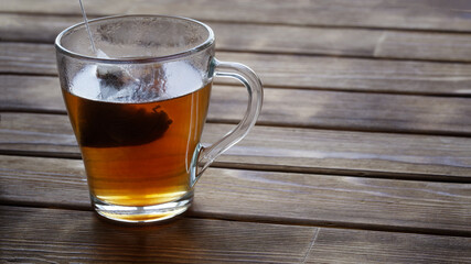 Black tea in a pyramid tea bag is brewed in boiling water in a transparent cup. Rustic background from natural pine boards. Free space for an inscription