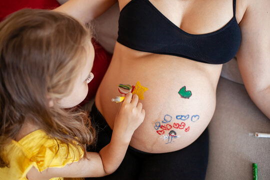 Cute little daughter painting on pregnant mother belly