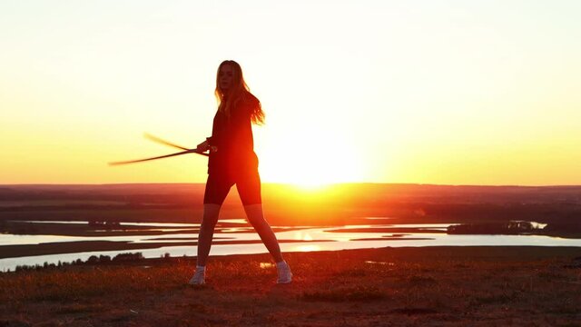 Swords training - young woman with long hair training with two swords on the background of the bright sunset