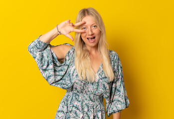 Portrait of a young smiling woman showing peace sign isolated on a yellow background