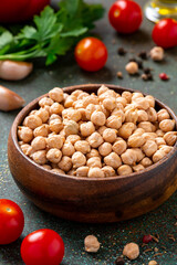 Dry uncooked chickpeas in a wooden bowl and ingredients for cooking on a dark background.