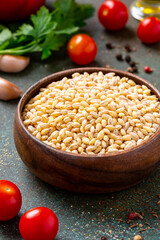 Dry uncooked pearl barley in a wooden bowl on a dark background close-up. 